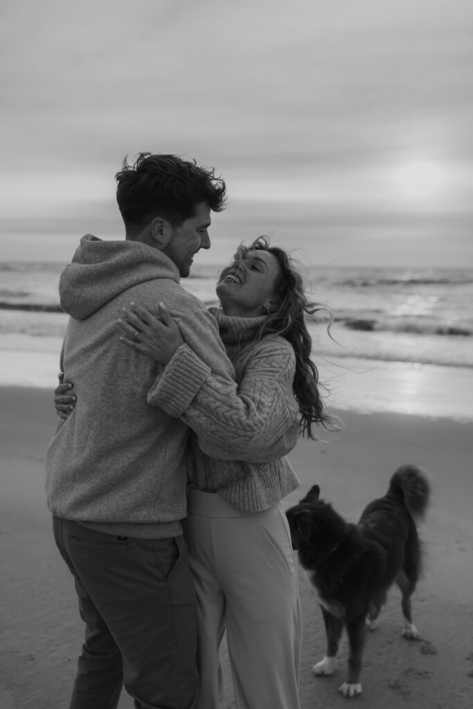 Paar am Strand, Bild schwarz-weiß, Meer und Wellen im Hintergrund, Hund steht hinter Paar