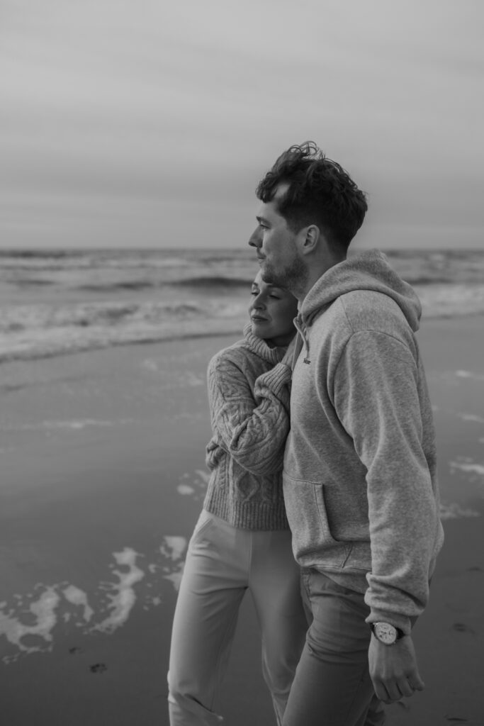 schwarz-weiß Bild von Paar am Strand, kuscheln, schauen auf Wellen